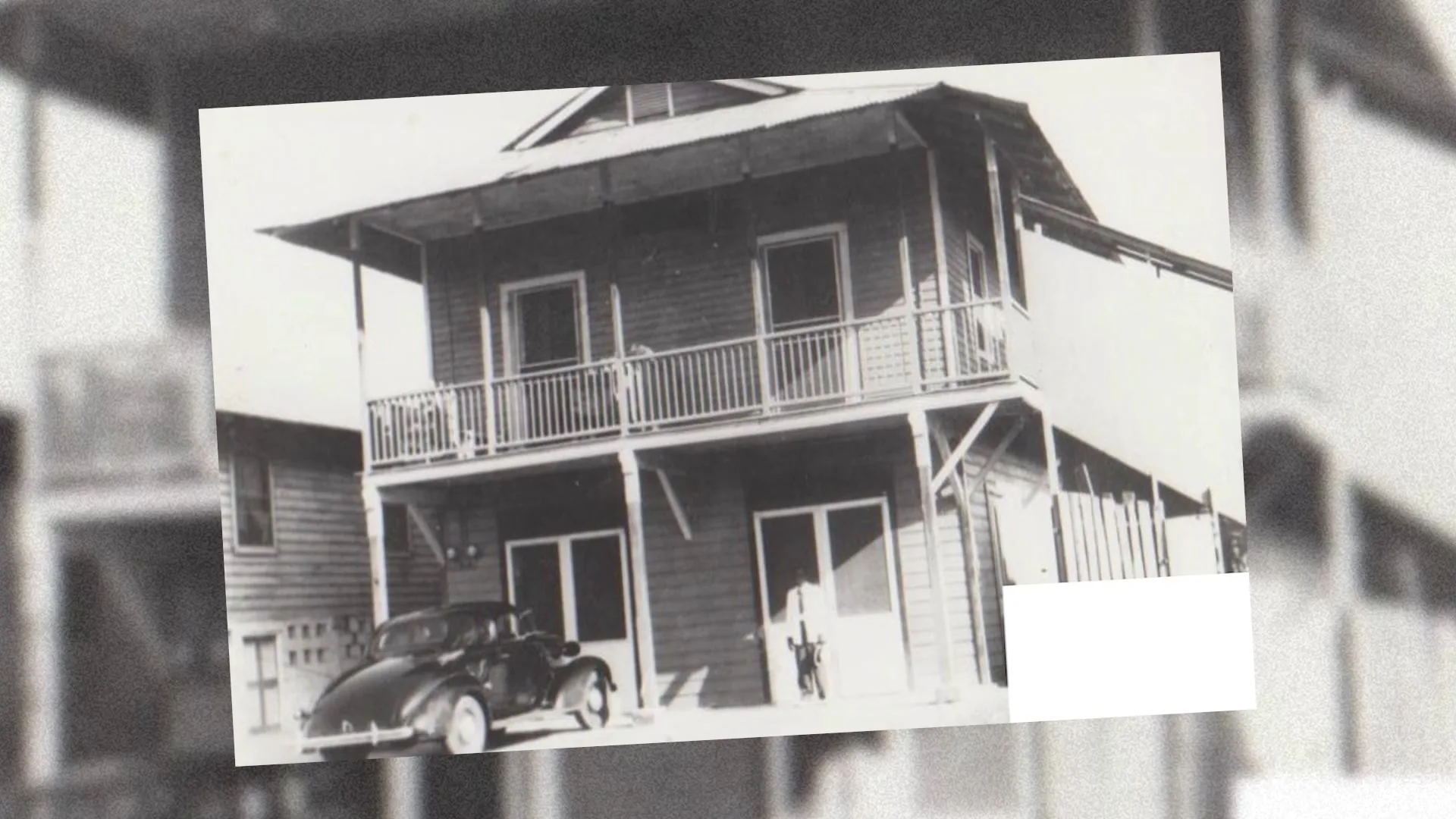 Fotografía histórica de un edificio de madera de dos pisos con un auto clásico al frente.