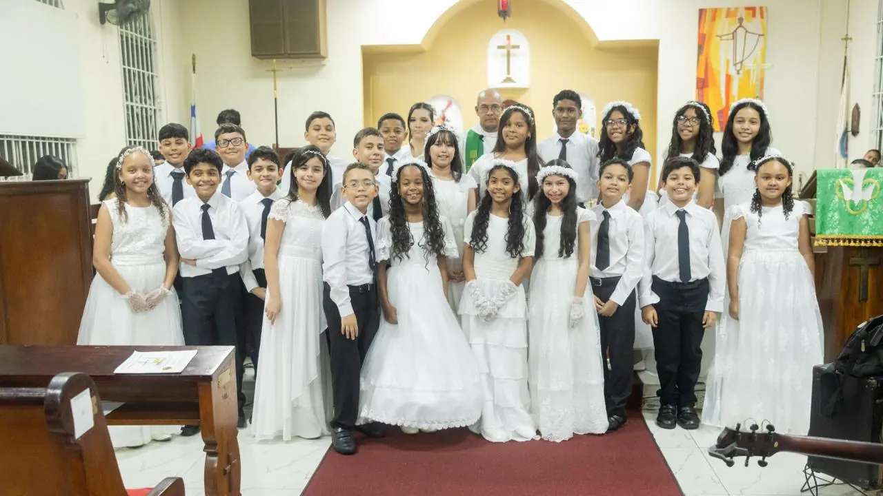 Fotografía grupal de los participantes de Primera Comunión junto al sacerdote frente al altar.